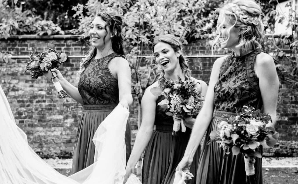 Bridesmaids holding up the Brides dress so it doesn't drag on the ground. Happy smiling Bridesmaids