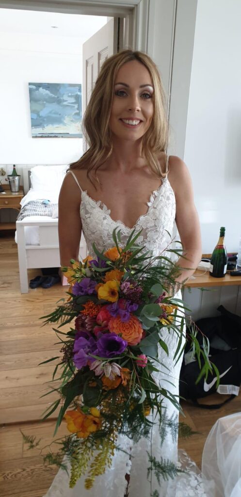 A happy bride with beachy hair, holding bright colourful flowers